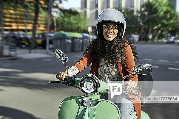 Lächelnde Frau auf einem elektrischen Motorroller in der Stadt an einem sonnigen Tag