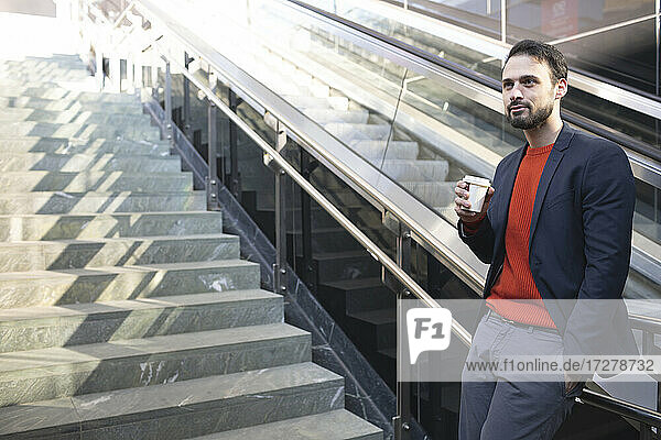 Selbstbewusster Geschäftsmann trinkt Kaffee  während er auf einer Treppe in der Stadt steht