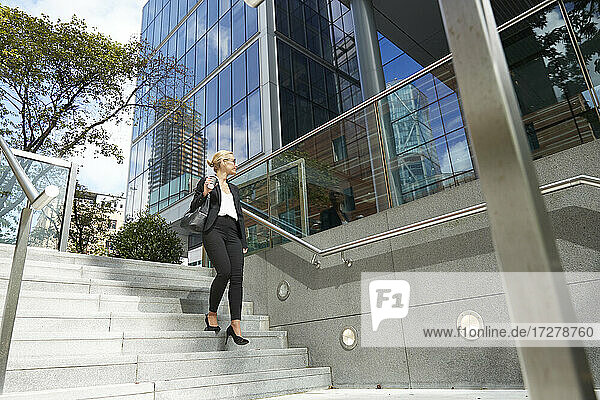 Geschäftsfrau schaut weg  während sie auf einer Treppe gegen ein Gebäude läuft