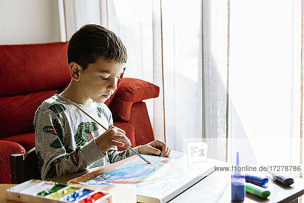 Junge malt in den Sommerferien zu Hause über den Tisch