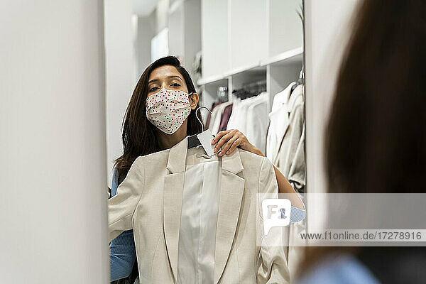 Frau trägt Schutzmaske  während sie die Reflexion ihres Anzugs im Spiegel eines Einkaufszentrums betrachtet