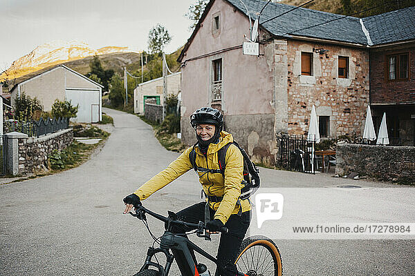 Mid adult woman in warm clothing riding mountain bike on road while traveling to Somiedo Natural Park  Spain