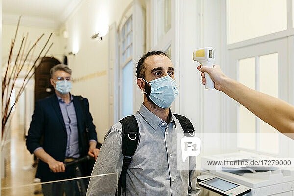 Frau mit Infrarot-Thermometer  die die Temperatur eines Geschäftsmannes im Korridor überprüft