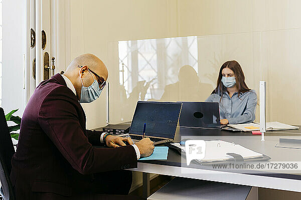 Männliche und weibliche Unternehmer mit Schutzmaske bei der Arbeit im Büro