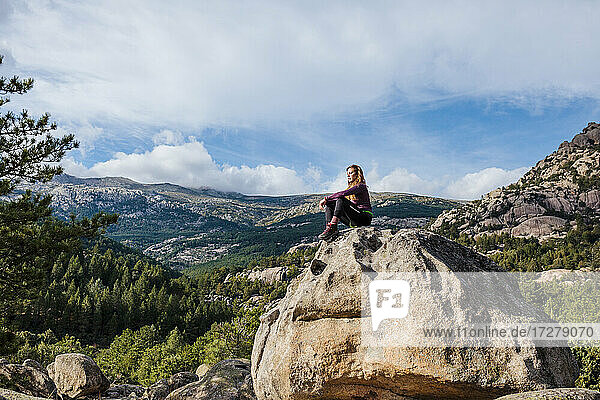 Wanderer betrachtet die Aussicht  während er auf einem Felsen gegen den Himmel in La Pedriza  Madrid  Spanien  sitzt