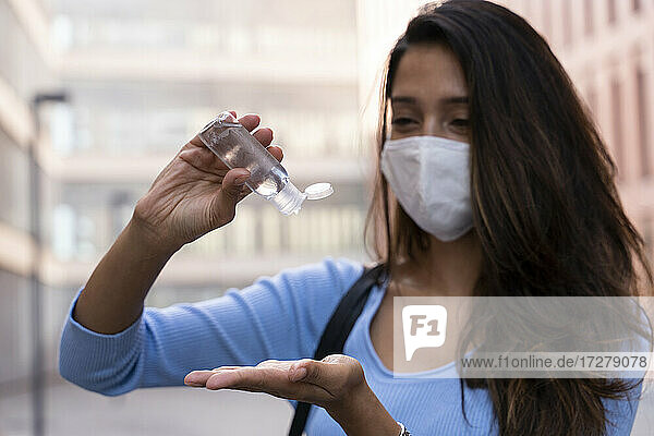 Geschäftsfrau mit Gesichtsmaske  die während der COVID-19 Desinfektionsmittel auf die Hand gießt