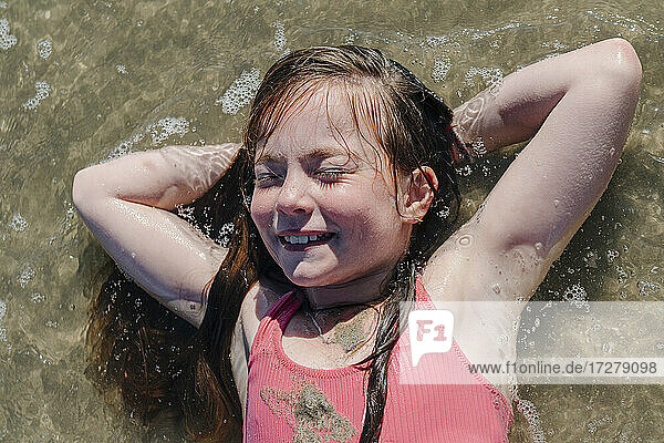 Mädchen auf dem Rücken liegend mit den Händen hinter dem Kopf im Wasser an einem sonnigen Tag