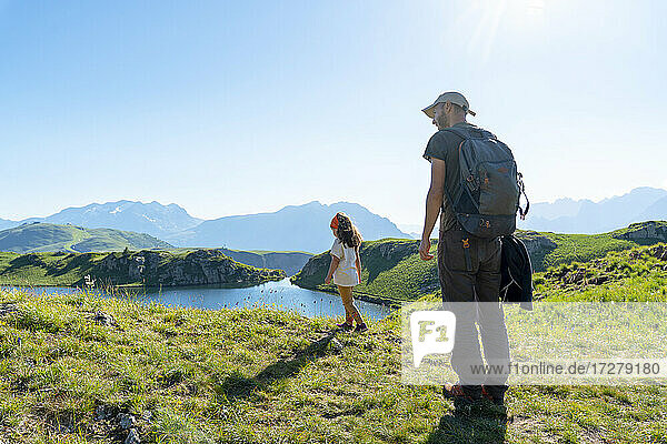 Vater und Tochter stehen auf einer Wiese und schauen auf einen See an einem sonnigen Tag