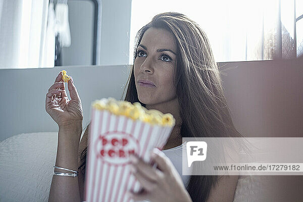Young woman eating popcorn while sitting at home