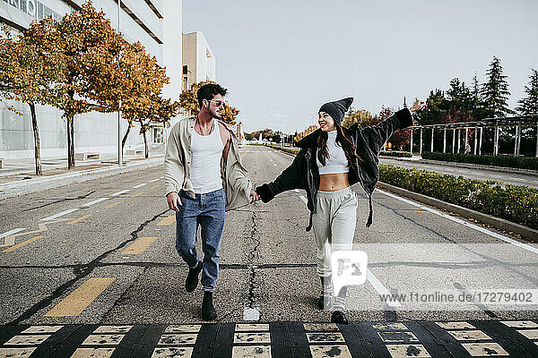 Beautiful smiling woman holding hands with male partner while walking on road in city