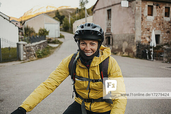Smiling mid adult woman in warm clothing riding mountain bike on road while traveling to Somiedo Natural Park  Spain