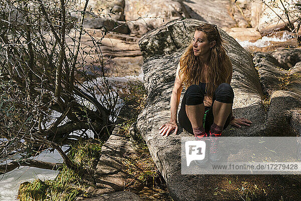 Frau schaut weg  während sie sich auf einem Felsen am Fluss im Wald von La Pedriza  Madrid  Spanien  ausruht