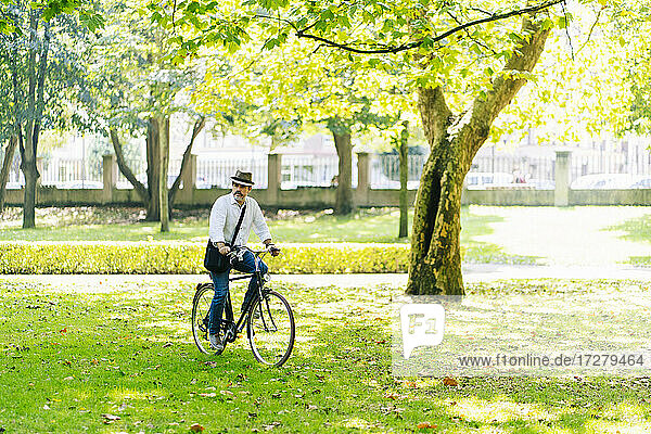 Älterer Mann  der an einem sonnigen Tag auf dem Rasen eines Parks Rad fährt
