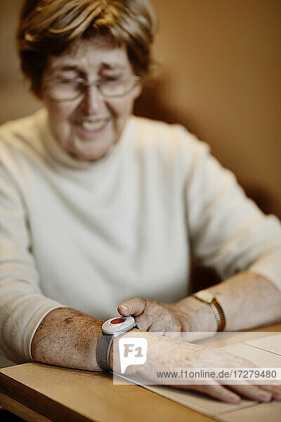Ältere Frau drückt Notrufknopf am Handgelenk über Tisch zu Hause