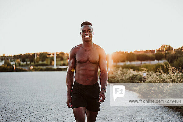 Smiling male athlete walking in park against sky during sunset