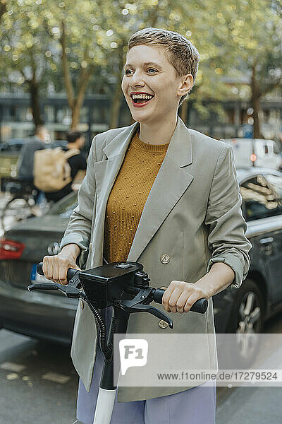Fröhliche Frau fährt mit einem elektrischen Roller auf der Straße in der Stadt