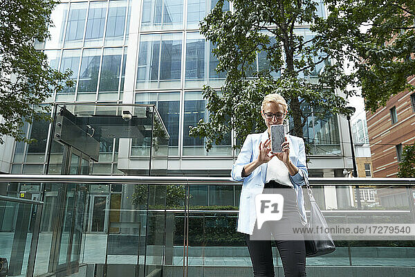 Reife Frau  die ein Mobiltelefon benutzt  während sie sich auf ein Geländer in der Stadt stützt