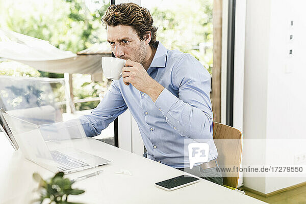 Man working on laptop while drinking coffee sitting in office