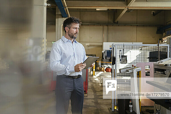 Geschäftsmann mit digitalem Tablet  der in einer Fabrik stehend Produktionsanlagen untersucht