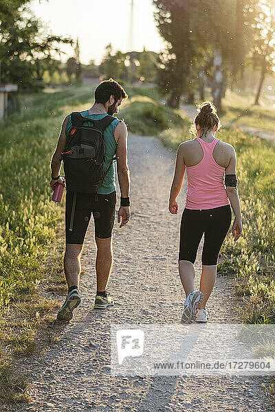 Aktives Paar in Sportkleidung beim Spaziergang im Park während des Sonnenuntergangs