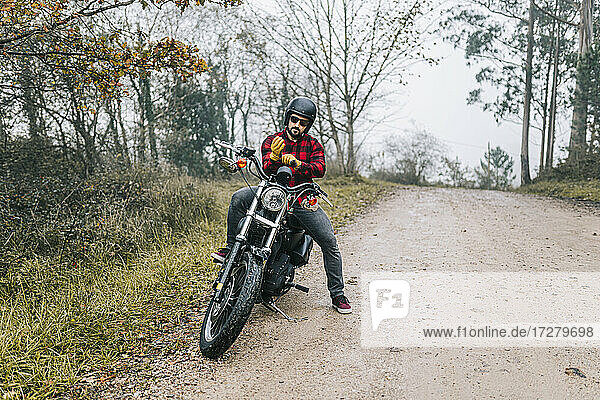 Männlicher Motorradfahrer mit Handschuhen auf dem Motorrad sitzend auf einem Feldweg