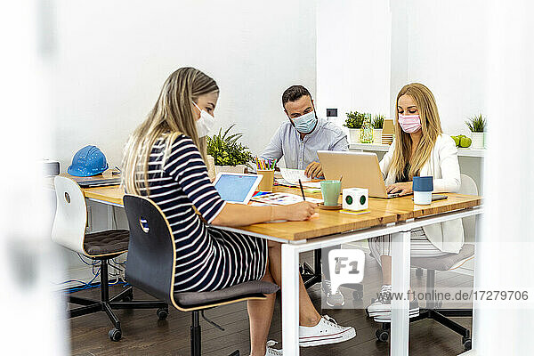 Geschäftsleute tragen Gesichtsmaske beim Sitzen am Schreibtisch im Büro