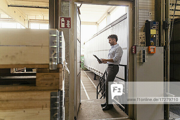 Älterer Mann benutzt ein digitales Tablet  während er neben einem Lieferwagen in einer Fabrik steht