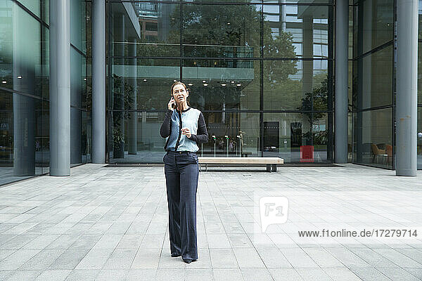 Frau  die mit einem Mobiltelefon spricht  während sie vor einem Bürogebäude steht