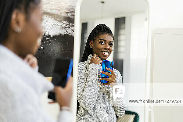 Lächelnde Frau nimmt Selfie durch Spiegelreflexion zu Hause