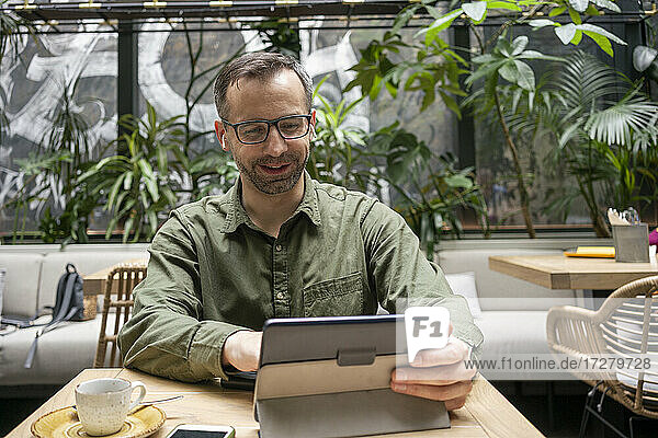 Lächelnder Geschäftsmann  der ein digitales Tablet benutzt  während er in einem Cafe sitzt