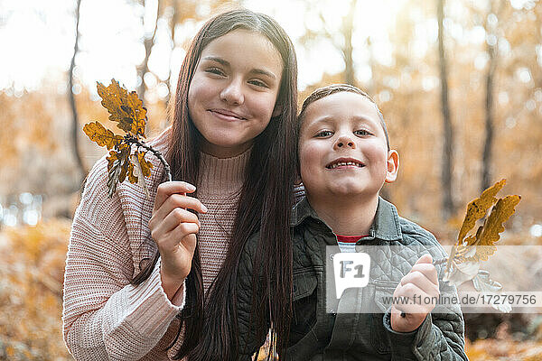 Bruder und Schwester halten im Herbst trockene Blätter im Park von Cannock Chase in der Hand