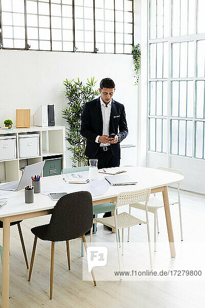 Männlicher Berufstätiger  der ein Smartphone benutzt  während er am Schreibtisch steht und im Büro arbeitet