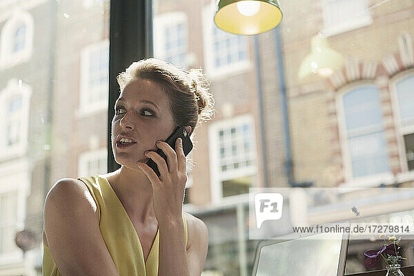 Junge Geschäftsfrau  die in einem Café mit einem Mobiltelefon spricht