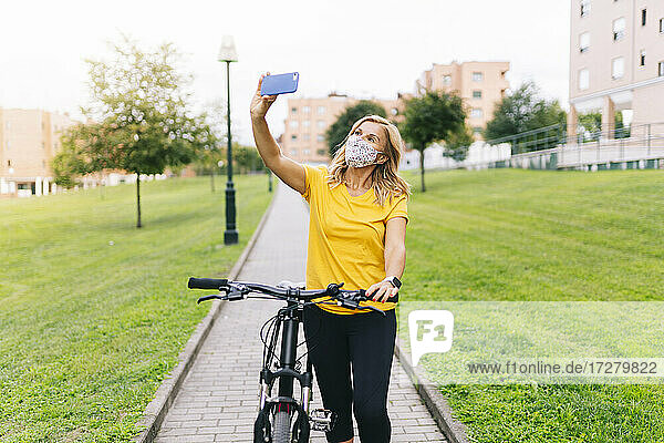 Frau macht Selfie mit Gesichtsschutzmaske auf einem Fußweg in der Stadt