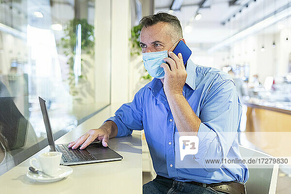 Businessman wearing protective face mask while talking on mobile phone at coffee shop