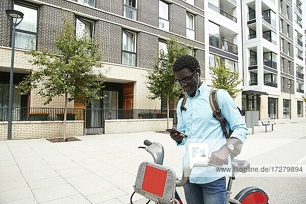 Mann mit Fahrrad stehend und Musik über Kopfhörer hörend auf der Straße in der Stadt stehend