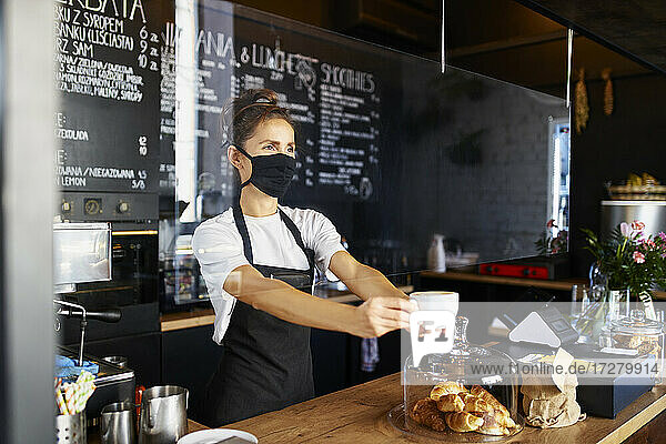 Waitress wearing protective face mask while giving coffee at cafe