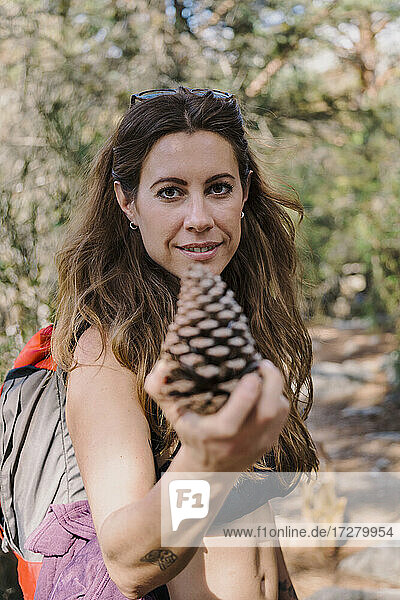 Smiling woman holding pine cone while standing at forest