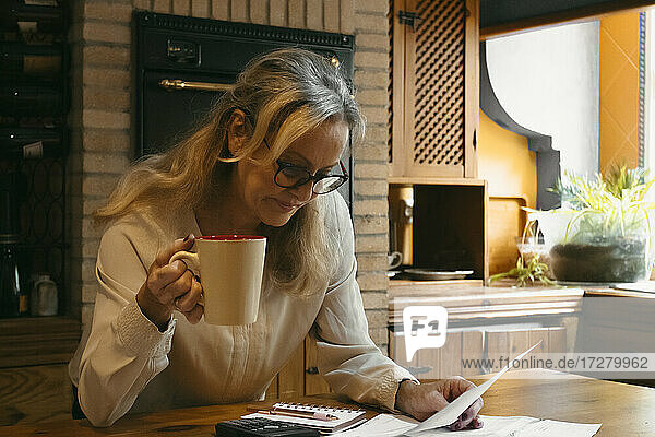 Frau trinkt Kaffee bei der Vorbereitung des Haushaltsplans im Stehen zu Hause