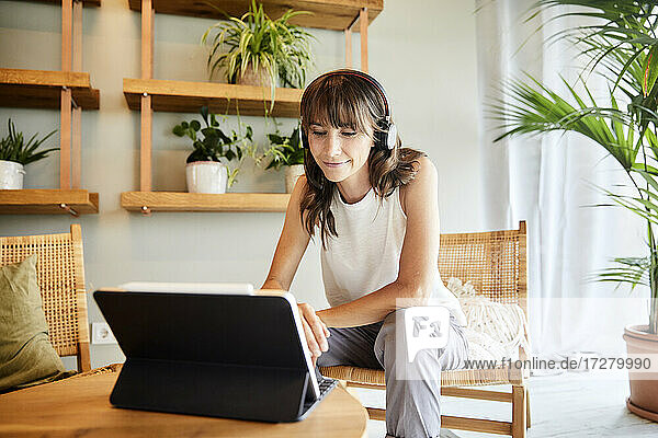 Frau hört Musik und benutzt ein digitales Tablet  während sie zu Hause sitzt