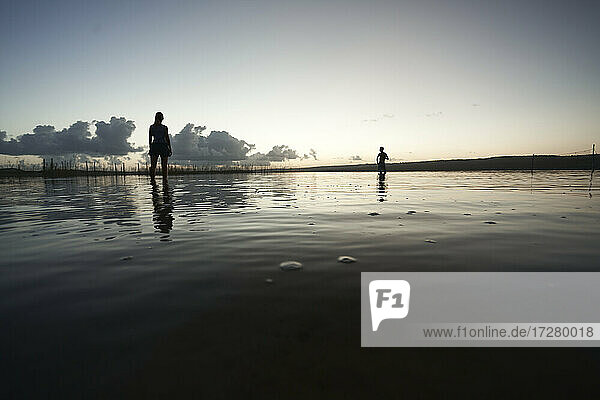 Silhouette Touristen am Strand mit Reflexion im Wasser gegen den Himmel bei Sonnenuntergang