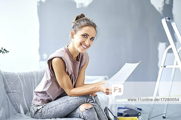 Lächelnde Frau liest Zeitung  während sie zu Hause auf dem Sofa sitzt