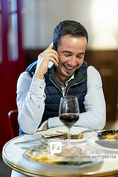 Junger Mann spricht am Esstisch eines Restaurants mit seinem Smartphone