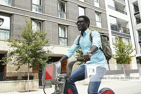 Lächelnder reifer Mann mit Rucksack beim Pendeln mit dem Fahrrad in der Stadt