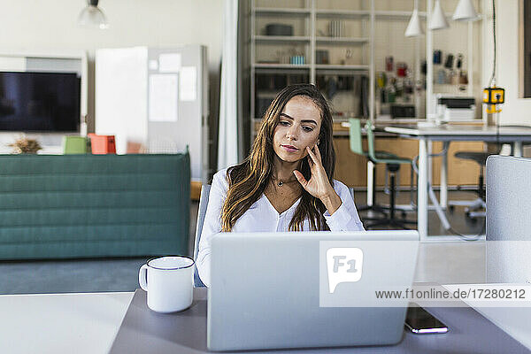 Geschäftsfrau denkt nach  während sie im Büro auf ihren Laptop schaut