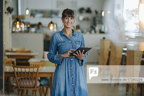 Smiling female entrepreneur using digital tablet while standing in coffee shop