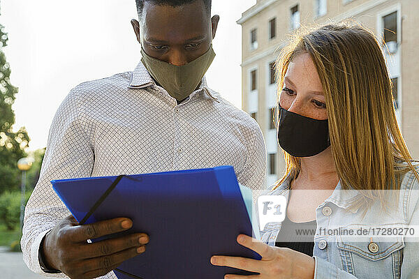 Männliche und weibliche Universitätsstudenten tragen einen Gesichtsschutz  während sie auf dem Campus diskutieren