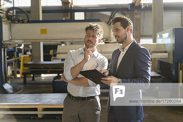 Businessmen with digital tablet looking away while standing at factory
