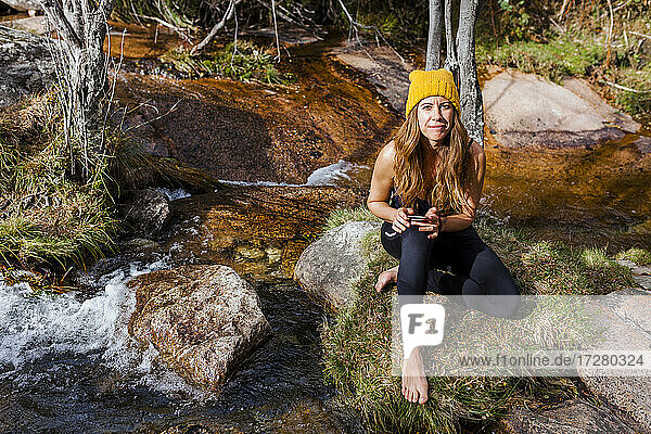 Forscher  der ein Mobiltelefon benutzt  während er am fließenden Wasser im Wald von La Pedriza  Madrid  Spanien  sitzt