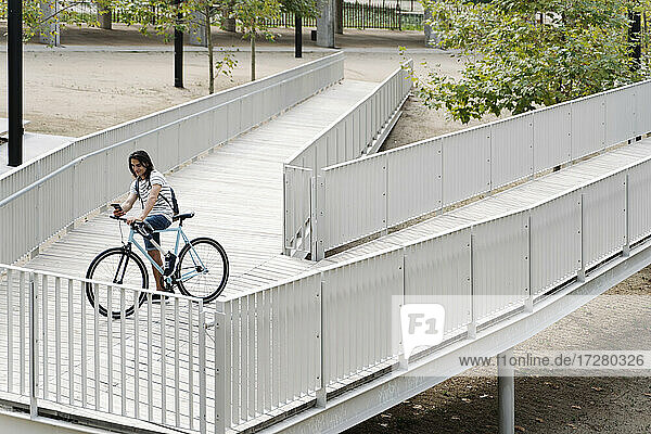 Hohe Winkel Ansicht der lächelnden amputierten Mann mit Handy auf dem Fahrrad über Brücke in der Stadt